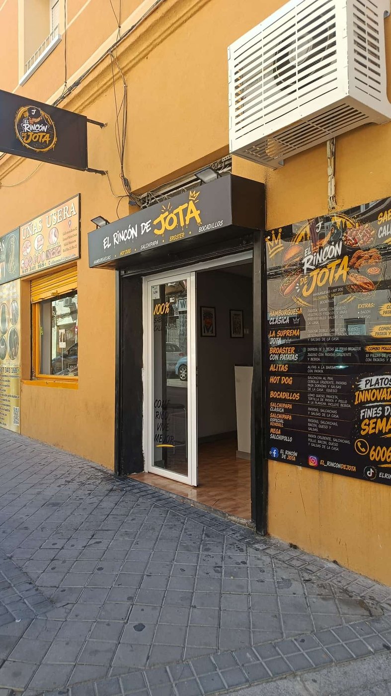Fachada de El Rincón de Jota en la calle Monederos 12 de Usera, con el rótulo del local y el cartel de la carta junto a la puerta.